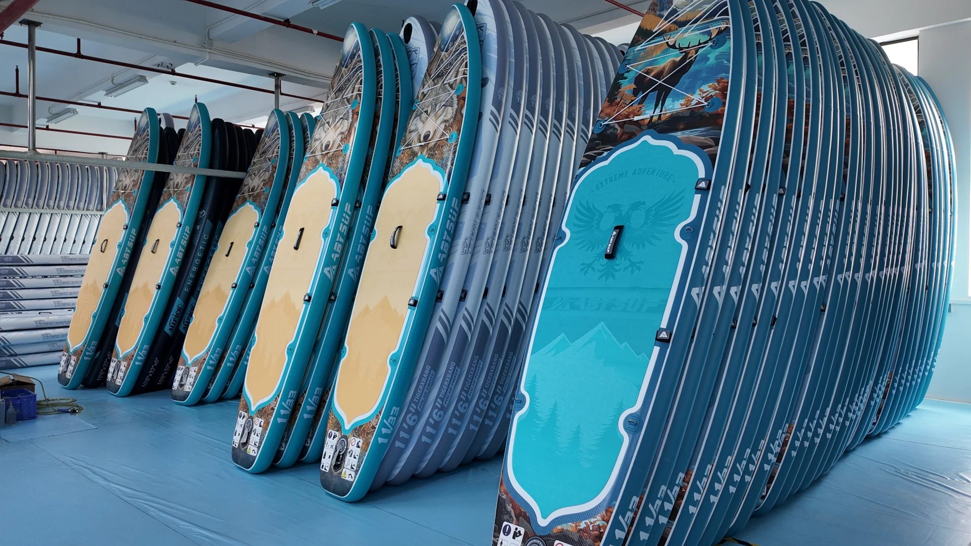 Rows of inflatable paddleboards neatly stacked in a warehouse setting, showcasing various designs and vibrant colors.