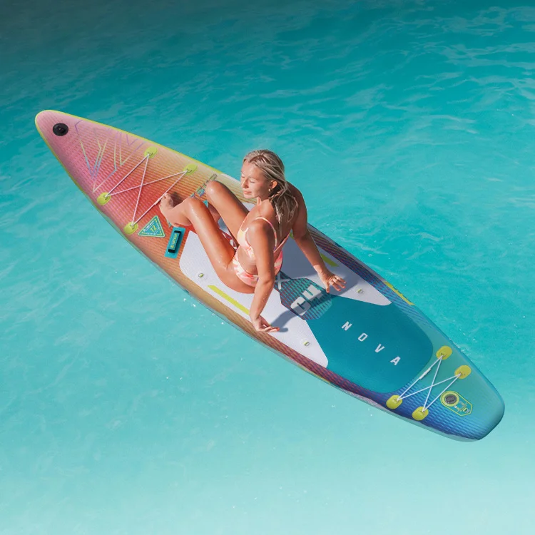 A woman in a bikini sitting on a colorful paddleboard in clear blue water.