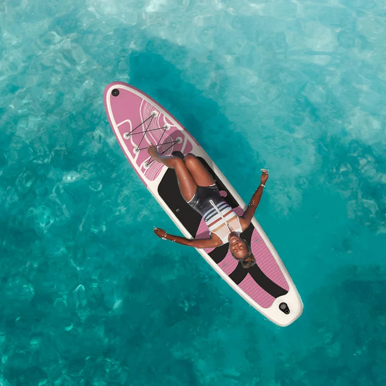 Woman in a swimsuit lounging on a pink paddleboard, floating on clear turquoise water, enjoying a sunny day.