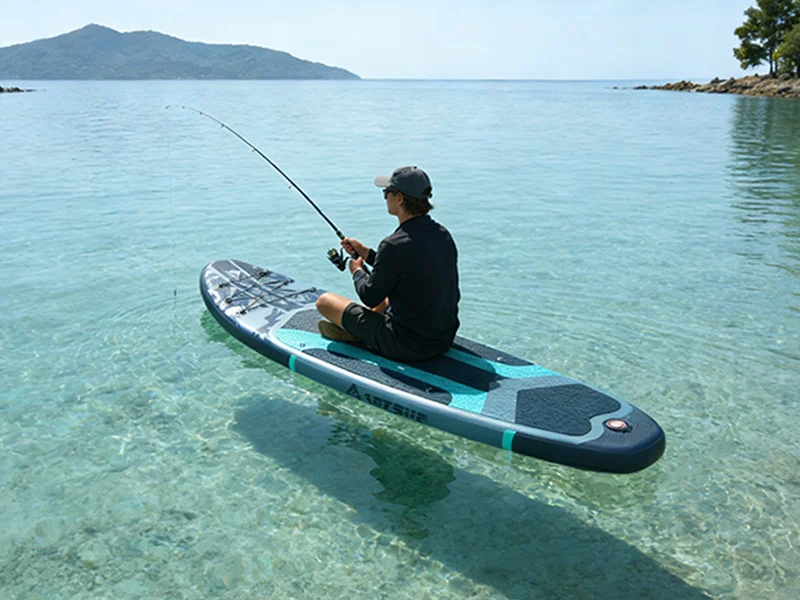 Man sitting on a paddleboard while fishing in clear, shallow water, with an island visible in the background.