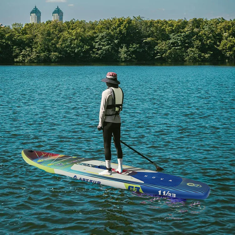 Person wearing a hat and life vest paddleboarding on a lake with a cityscape and trees in the background.