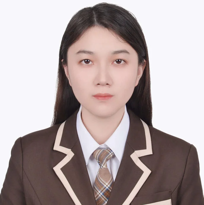 Individual wearing a brown suit with beige trim and plaid tie, showing upper body and part of the hair.