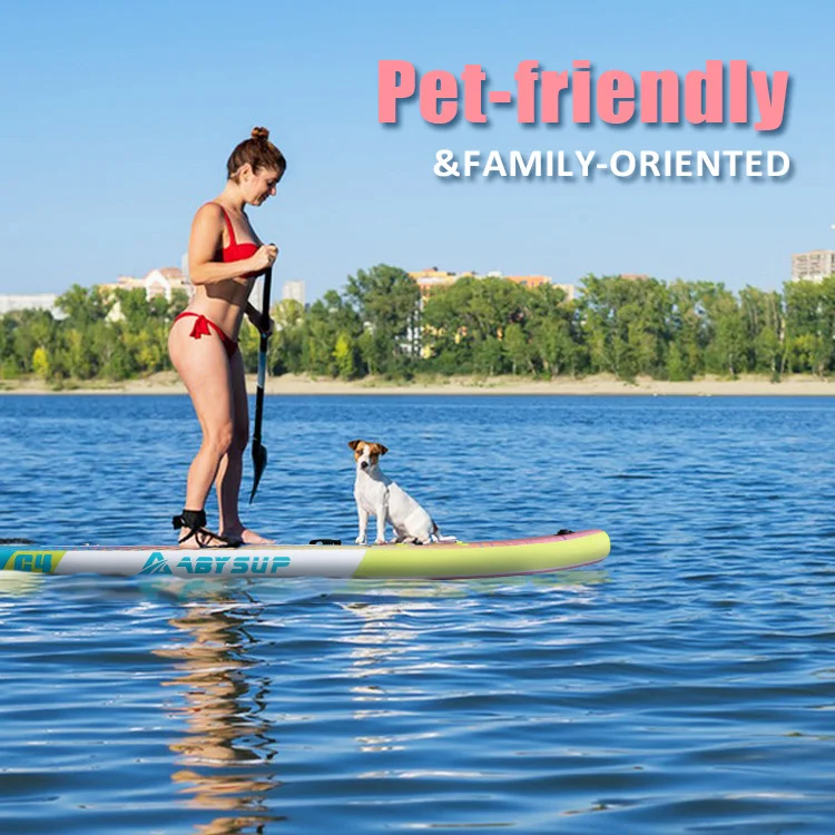 Woman in a red bikini paddleboarding on a calm lake with a small dog seated on the board, surrounded by trees and distant buildings.
