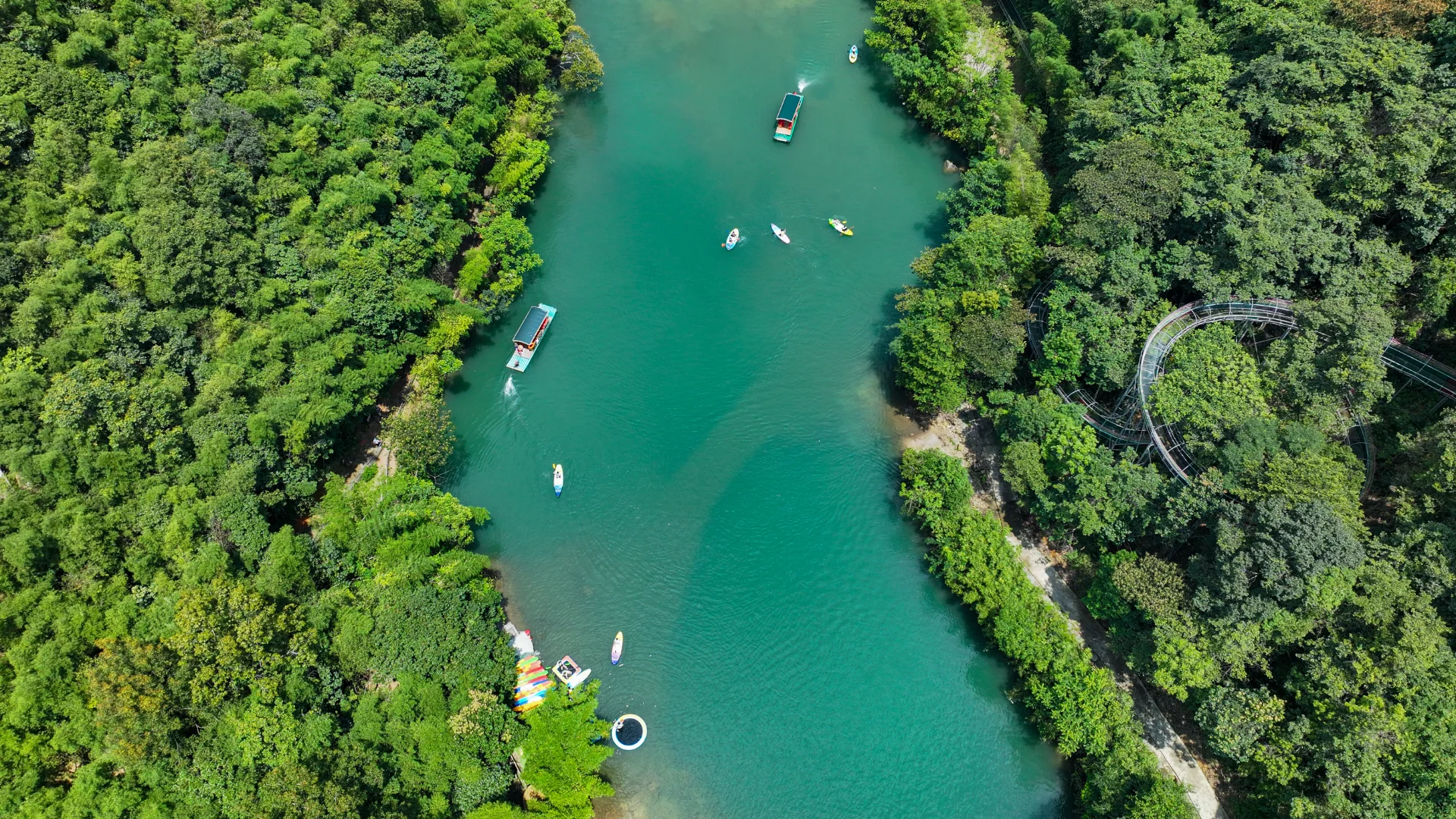 Aerial photograph of a river surrounded by dense greenery, featuring several boats and kayaks on the water.