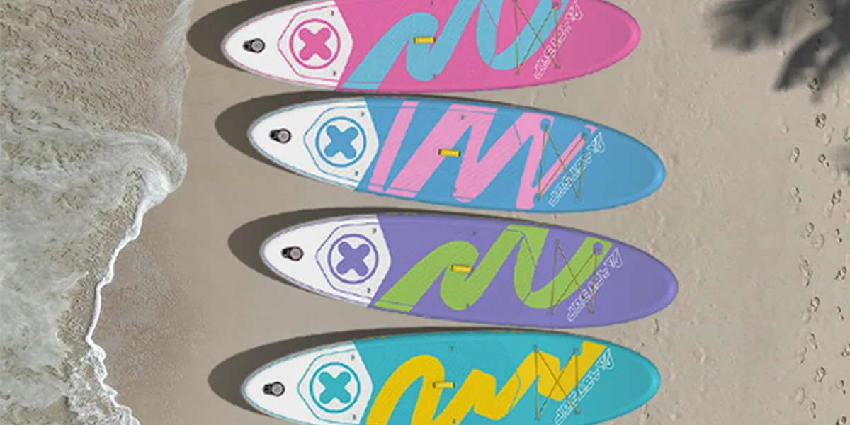 Four colorful paddleboards in pink, blue, purple, and turquoise arranged on a sandy beach near waves.