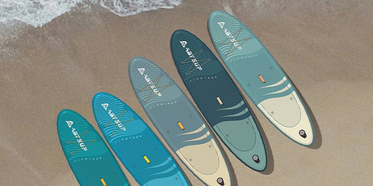 Five colorful surfboards laid out on a sandy beach near ocean waves.