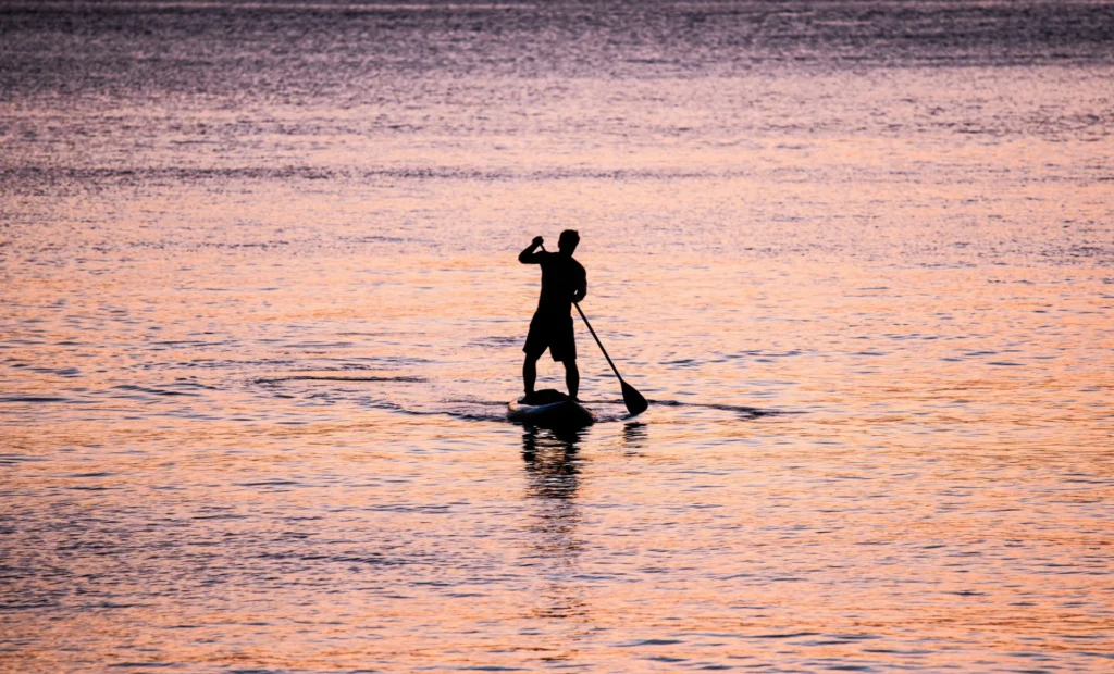 Silhouette of a person paddleboarding on calm water during a vibrant sunset.
