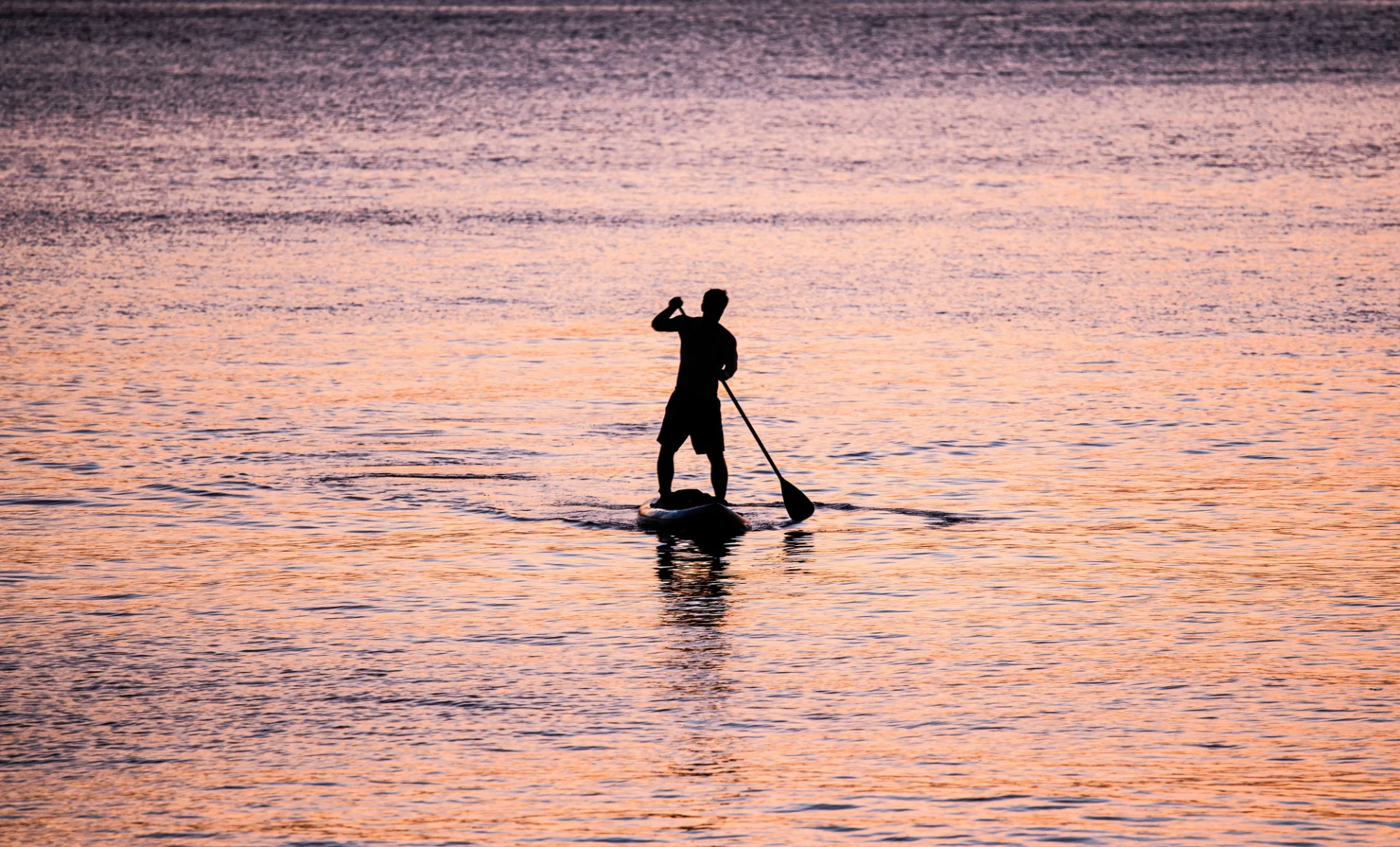 Silhouette of a person paddleboarding on calm water during a vibrant sunset.