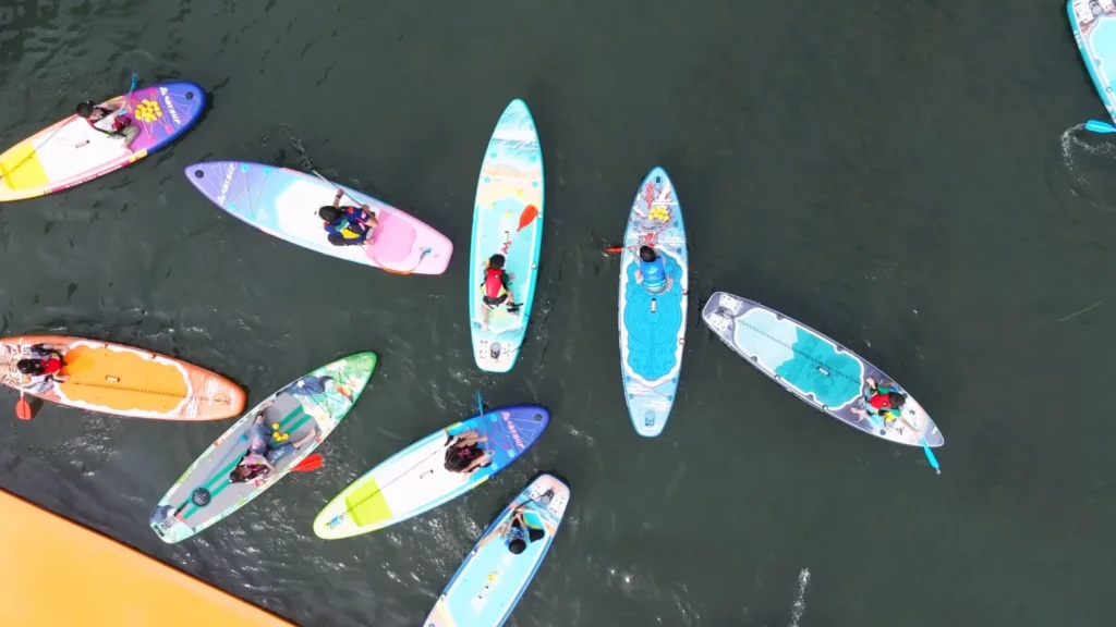 Top-down view of a group of paddleboarders floating on calm water, colorful boards, and individuals wearing life jackets.