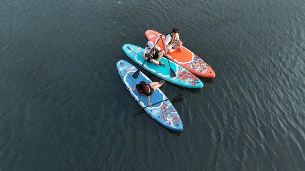 Three people paddleboarding on calm water using colorful boards, all wearing life jackets and holding paddles.