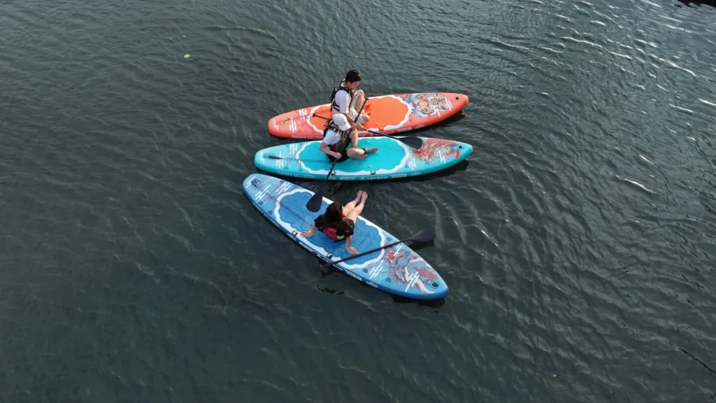 Three people paddleboarding on colorful boards floating on a calm lake, enjoying outdoor recreation.