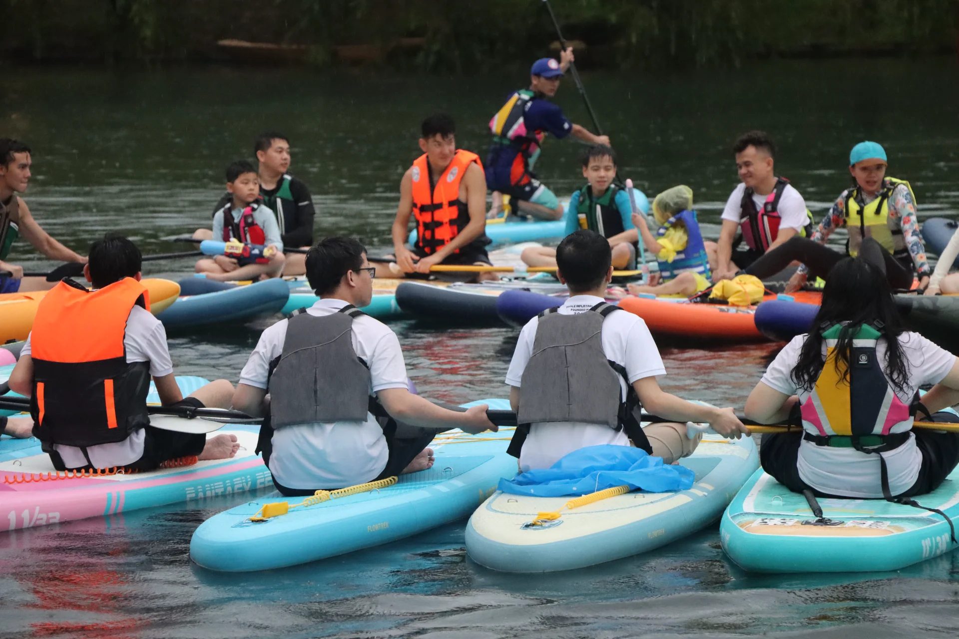 A group of individuals wearing life jackets on paddleboards gathered on a lake, engaging in recreational water activity.