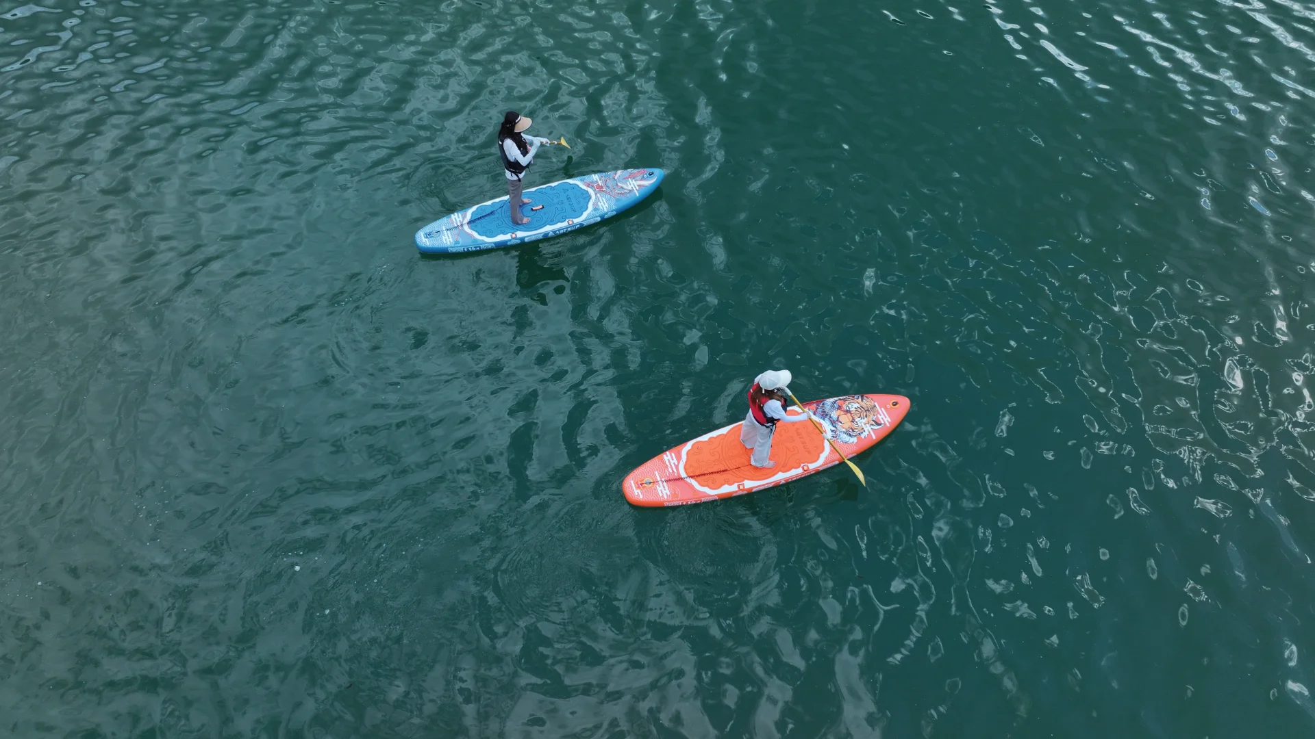 Two individuals on colorful paddleboards on calm water, each holding a paddle, enjoying an outdoor activity.