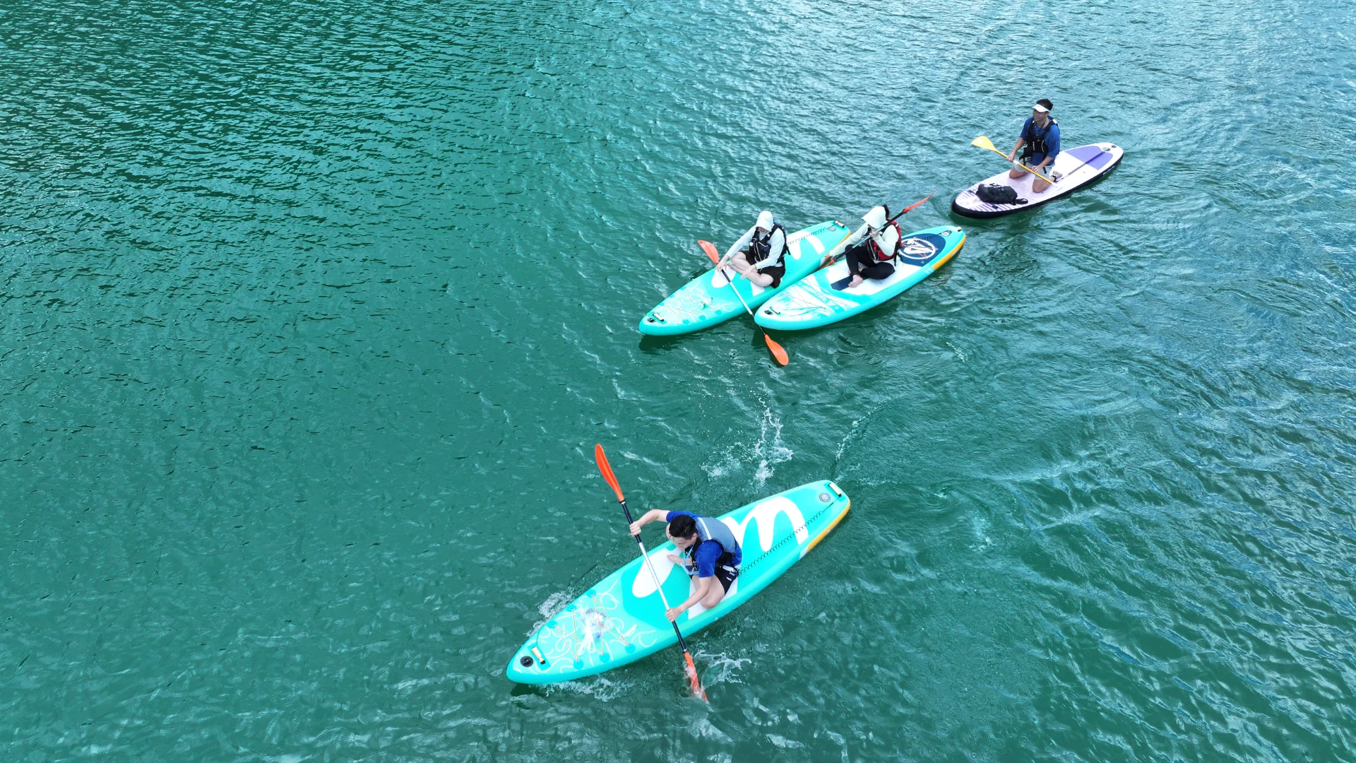 Group of three people paddleboarding on a serene, turquoise lake, each with stand-up paddleboards and safety gear.