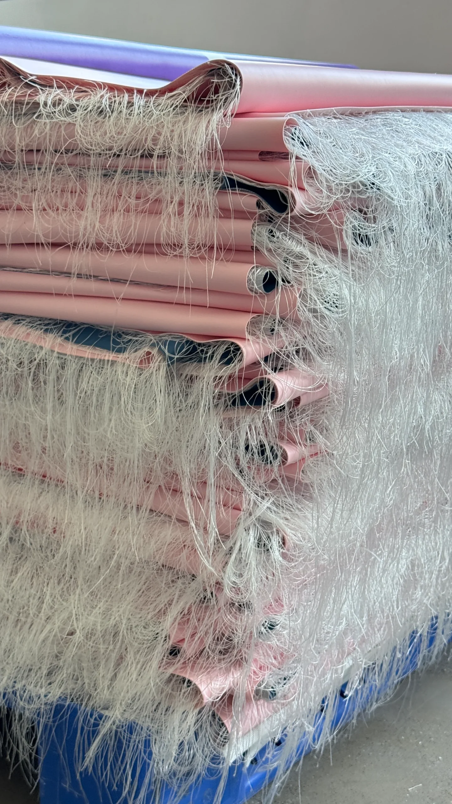 Close-up view of multiple stacked rolls of pink material with loose white fiberglass fibers exposed at the edges.