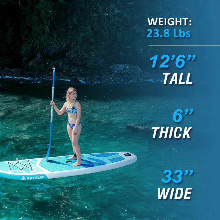Woman in a swimsuit standing on a paddleboard in clear, turquoise water with forested rocks in the background. Dimensions of the paddleboard displayed: 12'6'' tall, 6'' thick, and 33'' wide.